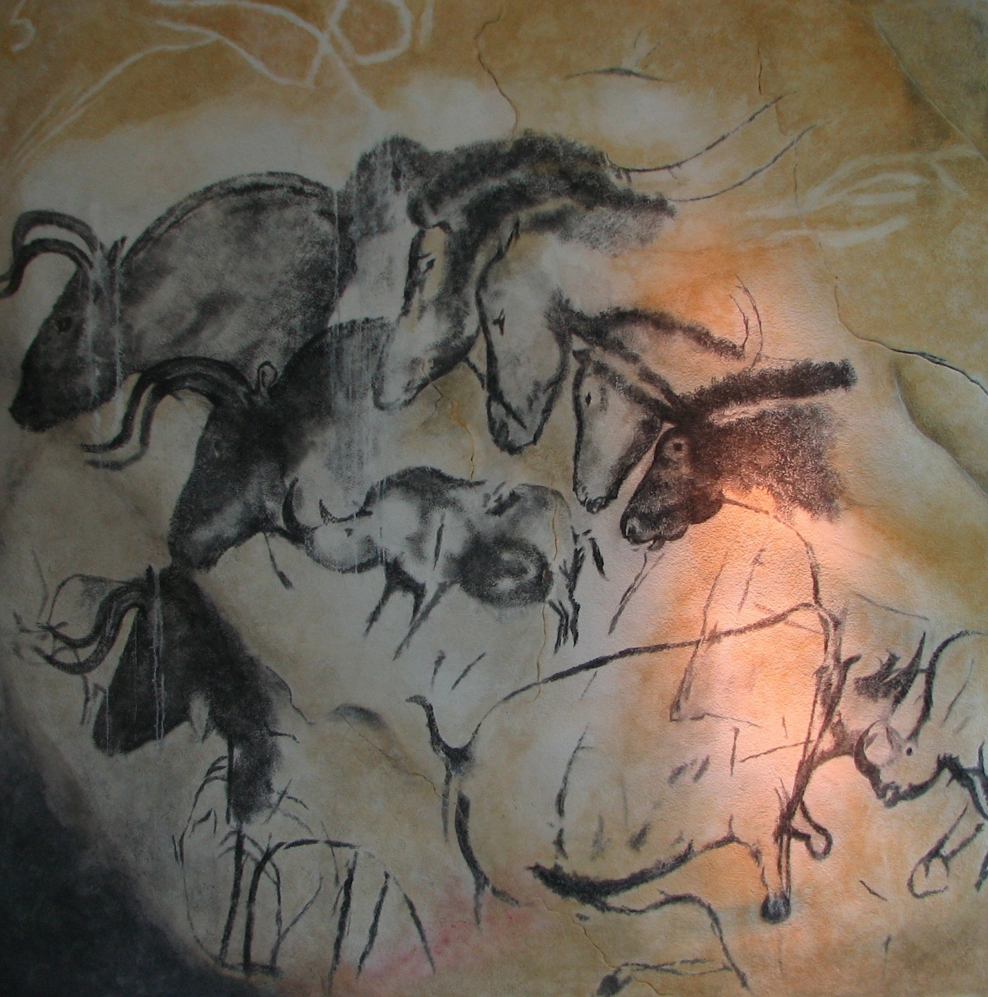 Photograph of prehistoric cave painting depicting a group of animals, including horses and bison, drawn with black and brown pigments on a textured rock surface. The artwork shows detailed animal features and movement, highlighting early human artistic expression and wildlife representation.