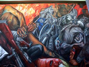 A mural painting depicting a chaotic battle scene with intertwined human and robotic figures, emphasizing struggle and conflict. The artwork features vivid colors, detailed expressions, and mechanical elements, highlighting themes of war, resistance, and technological oppression.