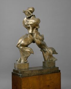 Photograph of an abstract bronze sculpture depicting a dynamic, fragmented human figure in motion, mounted on a wooden pedestal. The sculpture features angular, flowing shapes and exaggerated limbs, emphasizing movement and energy in a Futurist style.
