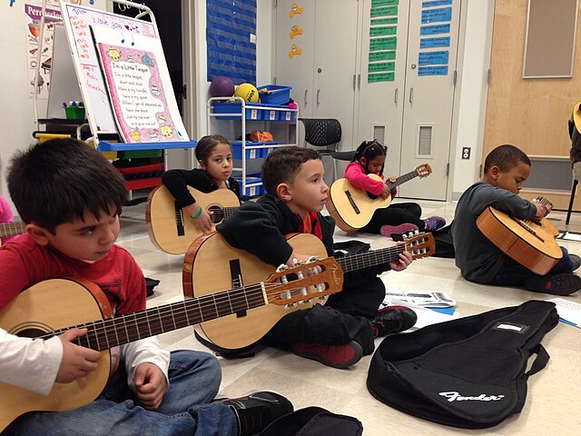 Children sitting on the floor, holding a guitar.