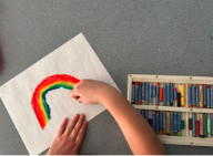 A child drawing a rainbow with colored pastels.