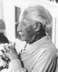 Black and white profile of an older man sitting with his hands clasped in front of him.