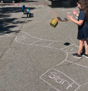 Girl throwing a large foam dice to move on an outdoor chalk drawn game board