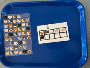 Hands placing cat stickers on a card with grid squares.
