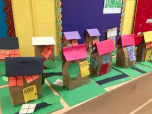 A series of paper bags placed on green paper resembling houses