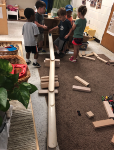 5 young children setting up a ramp with blocks and cars