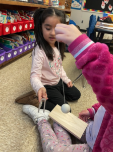 One child holding a ball on a string while another hits the ball with a tuning fork