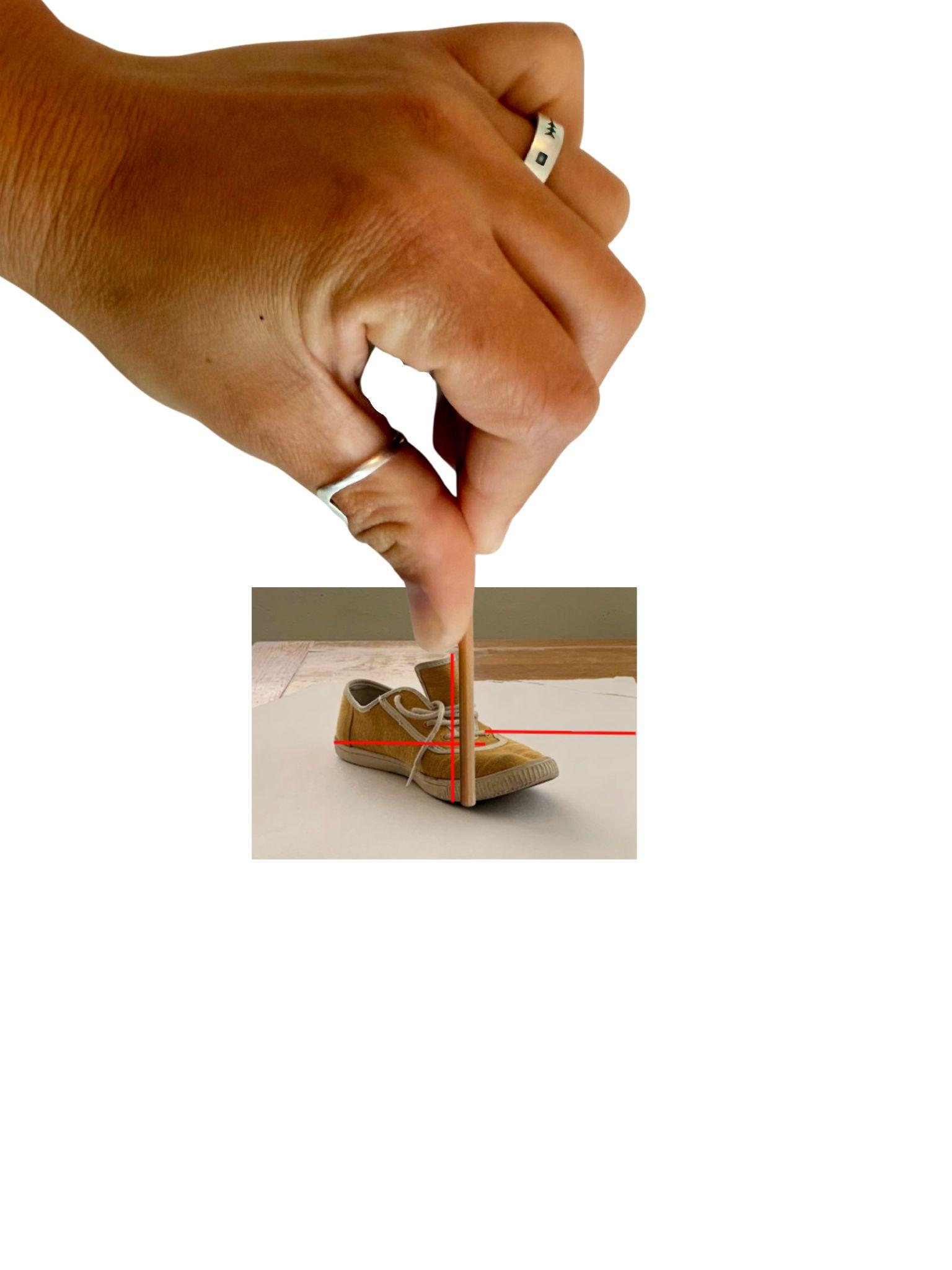 Photograph showing a large hand holding a sighting tool above a photograph of a brown shoe. The photograph of the shoe has two horizontal red lines and one vertical red line to highlight proportion comparison.