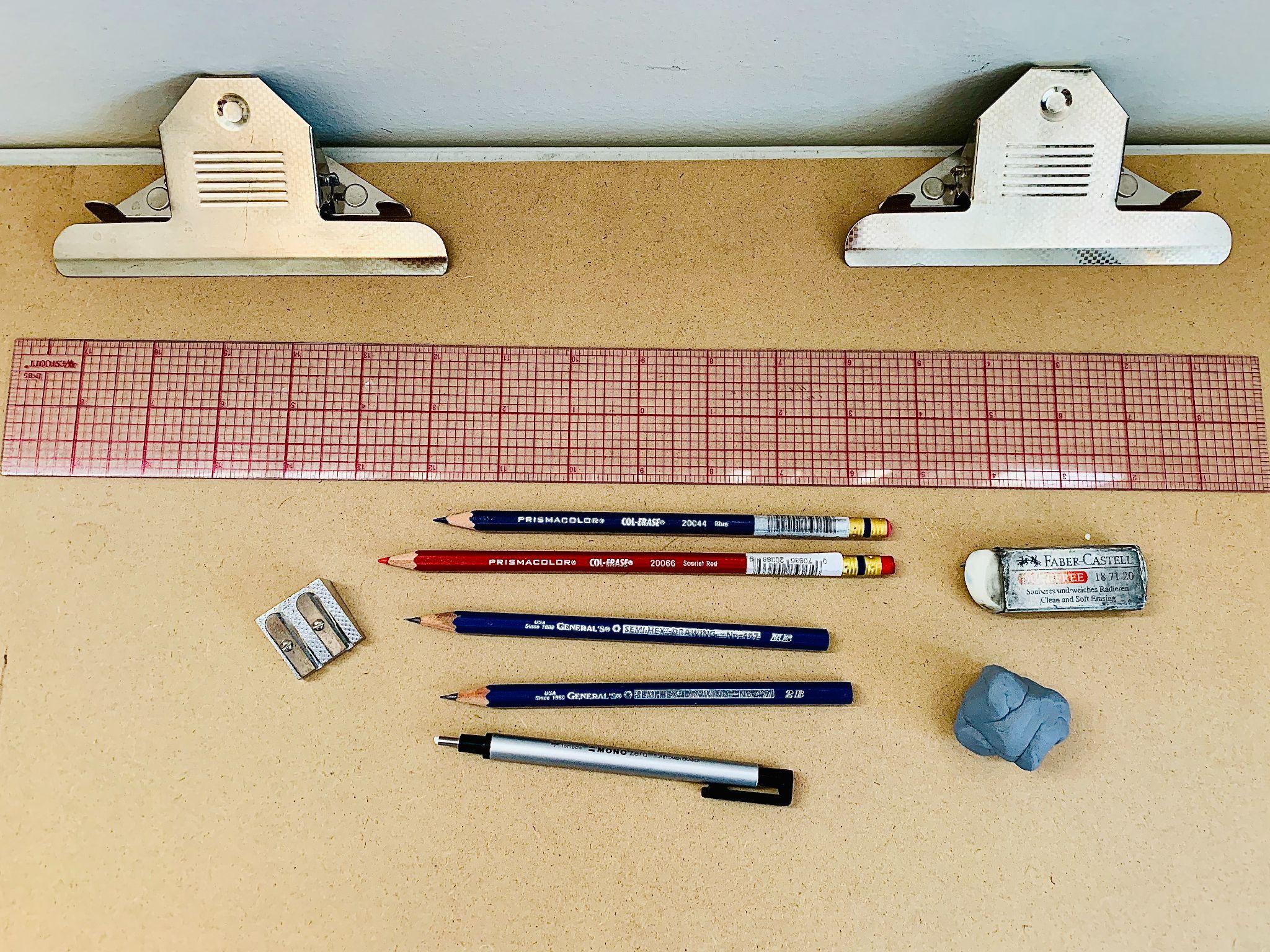 Photograph of various drawing tools arranged on a beige surface, including a red grid ruler, two metal clips, two sharpened pencils, two blue pencils, a mechanical pencil, a pen, a white eraser, a blue kneaded eraser, and a double pencil sharpener. Tools are neatly aligned, showcasing items commonly used for sketching.