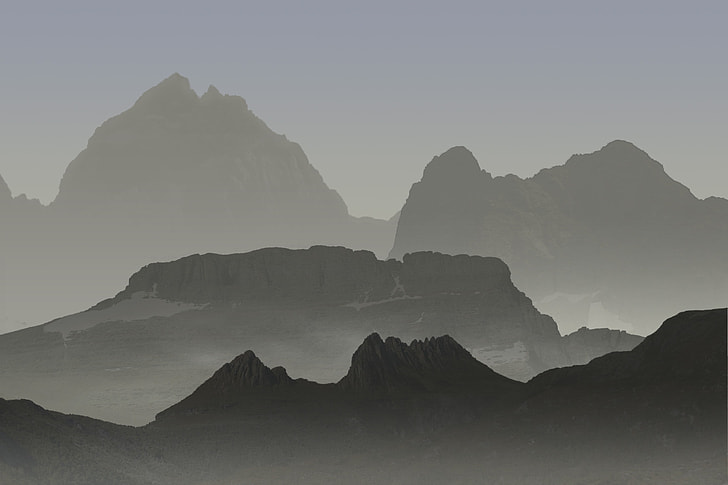 Photograph of a mountain range with multiple layers of peaks fading into the distance, creating a gradient of gray tones from dark in the foreground to light in the background. The scene captures atmospheric perspective and mist, emphasizing depth and rugged terrain.