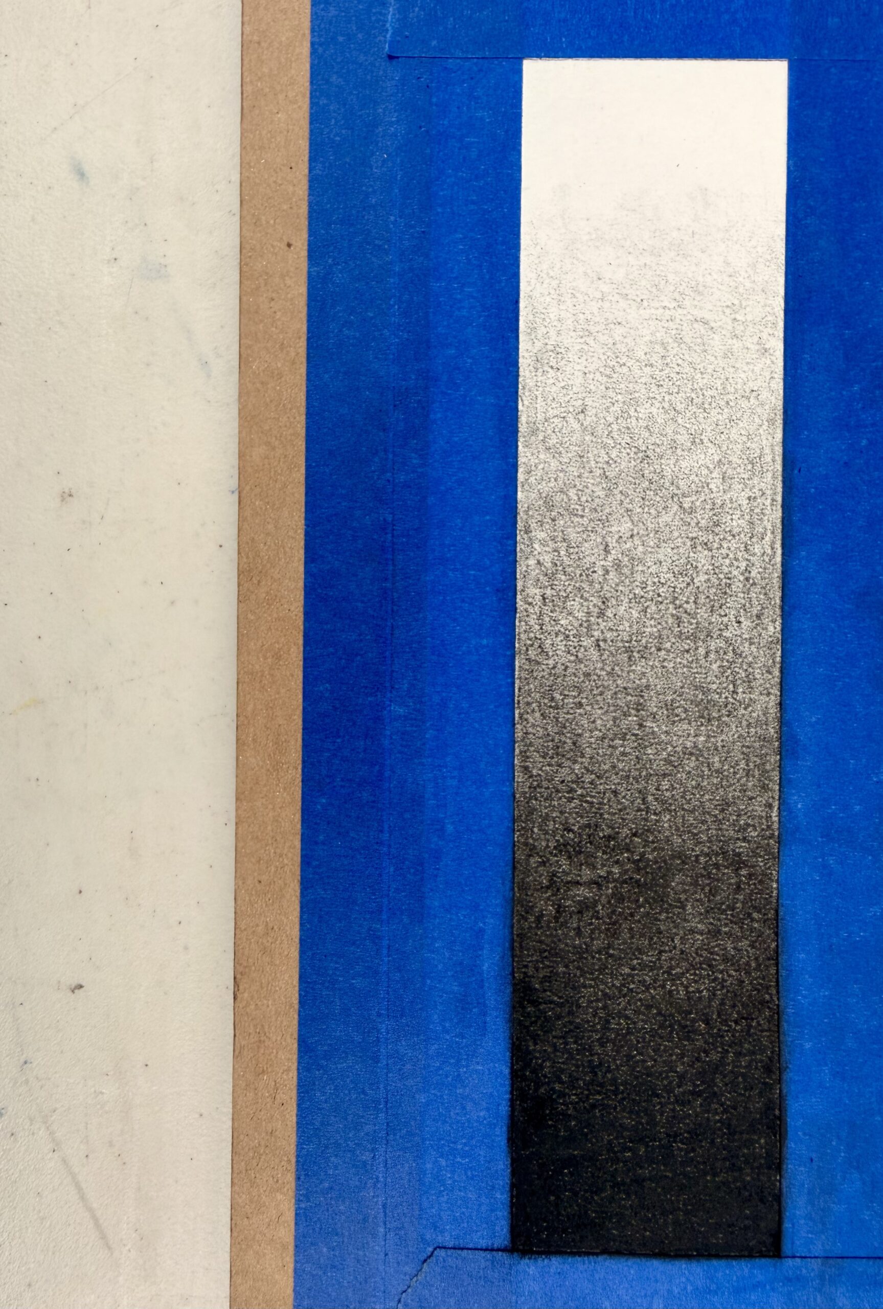 Photograph of a rectangular gradient transitioning from white at right to black at left, bordered by blue painter's tape. The gradient demonstrates smooth tonal variation, likely used for shading techniques.