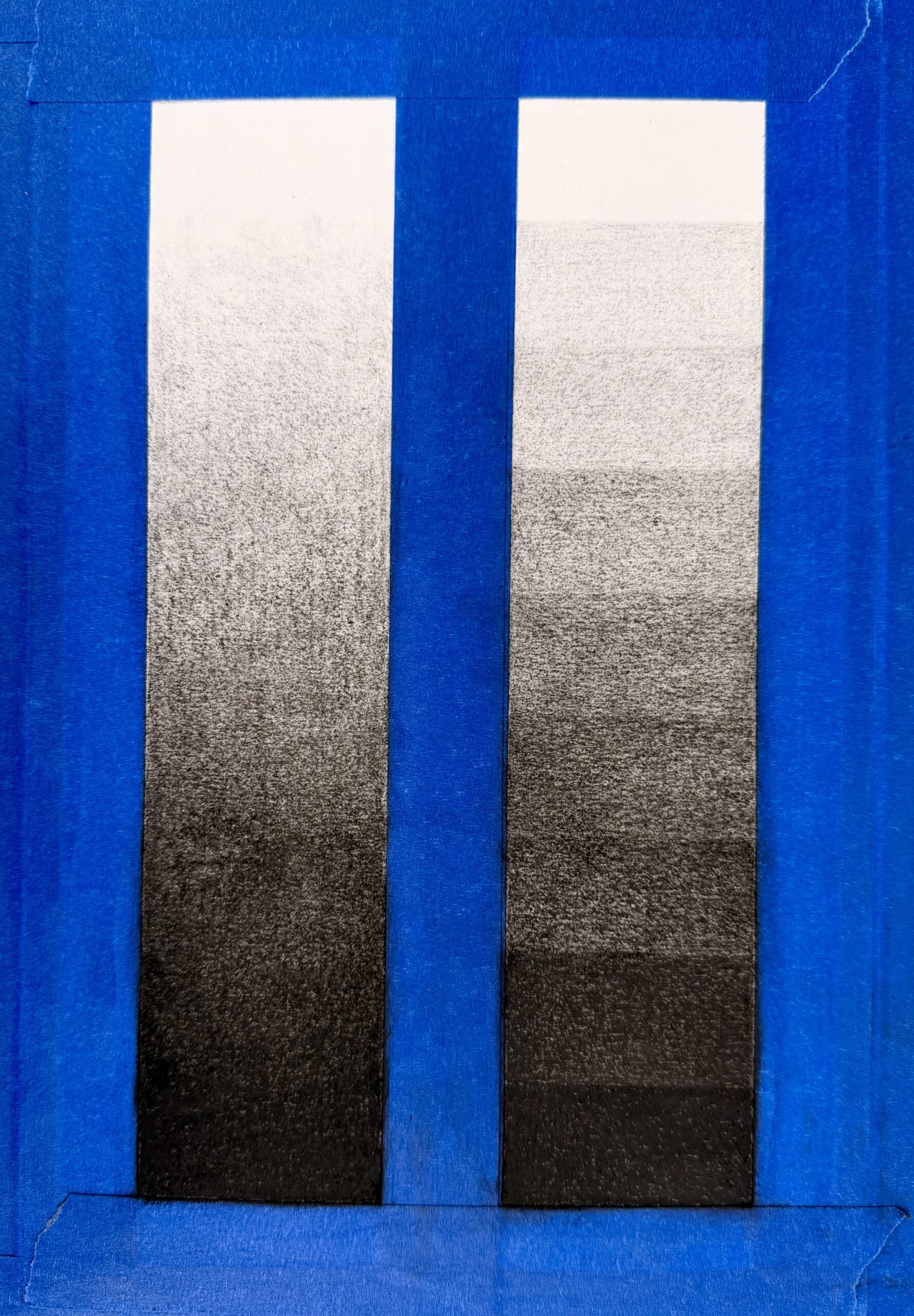 Photograph of two grayscale gradient strips side by side, bordered by blue tape on a blue background. Top strip shows a smooth continuous gradient from black at bottom to white at top, while bottom strip displays distinct horizontal bands transitioning from black to white.
