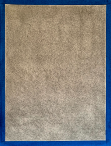 Photograph of a textured gray rectangular sheet centered on a blue background. The sheet has a fibrous, slightly mottled surface with no visible text or markings.