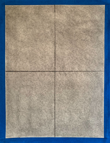 Photograph of a rectangular sheet divided into four equal quadrants by two intersecting black lines, placed on a blue background. The sheet has a textured gray surface with subtle variations in shading across each quadrant.