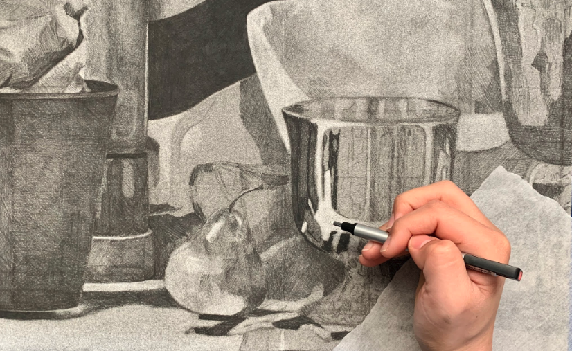 A photograph shows a hand using a mono eraser to do reductive drawing on a still life featuring reflective metal cups, a pear, and various textured objects. The artwork highlights intricate shading, reflections on the metal surfaces, and realistic textures, demonstrating advanced drawing techniques.