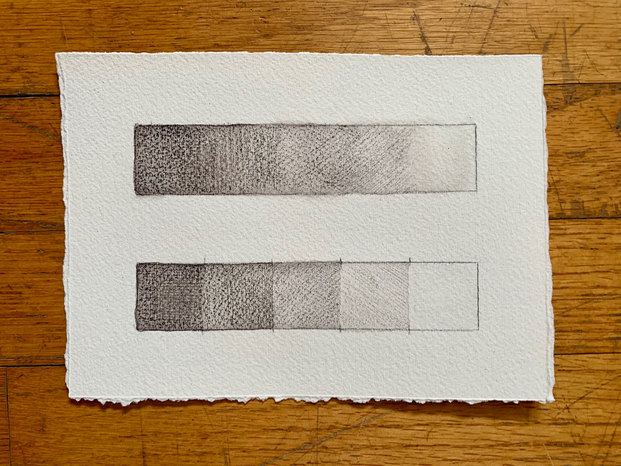 Photograph of two hand-drawn rectangular gradients on textured white paper. Each gradient transitions from dark to light shading, with the top gradient as a continuous smooth fade and the bottom divided into five distinct shaded sections.