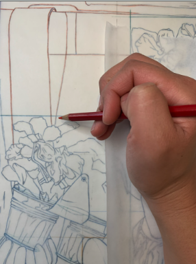 Photograph of a hand holding a red pencil, tracing or drawing a detailed floral sketch on translucent paper. The artwork features potted flowers with intricate petals and leaves, with some parts outlined in brown and others in blue pencil.