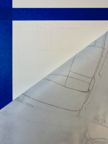 Photograph showing a close-up of a corner of a drawing or blueprint partially covered by a translucent sheet with hand-drawn lines. The background features a blue surface with a horizontal white stripe near the top.