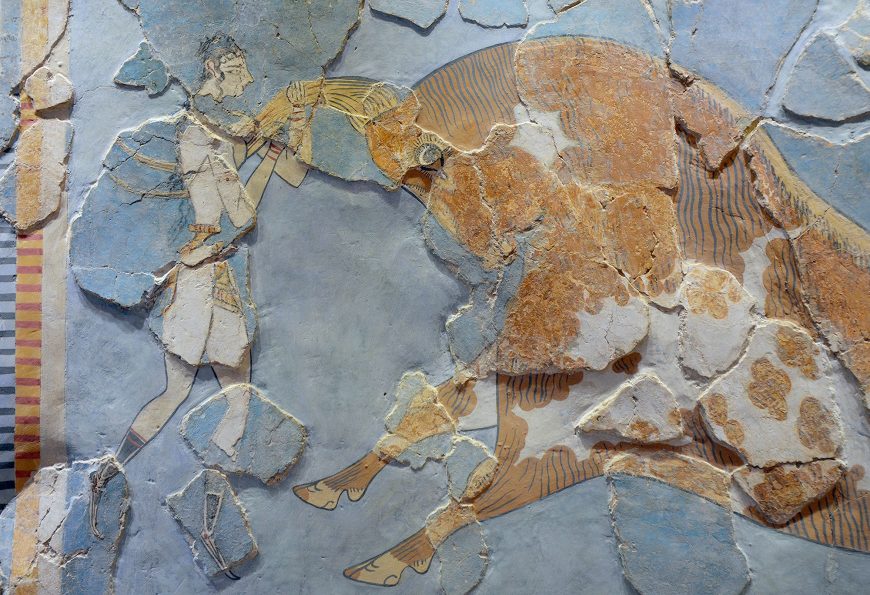 Bull-leaping fresco (detail) depicting a man holding the horn of a large bull, showcasing dynamic interaction between human and animal. The artwork features earthy tones with detailed line work on the bull's body and a fragmented background with visible cracks and missing sections.