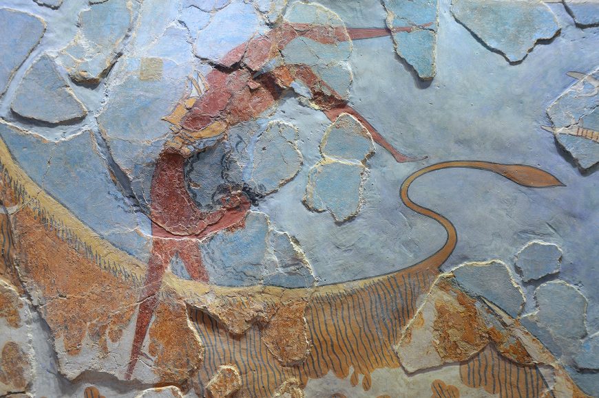 Bull-leaping fresco (detail) showing the male figure in a hand-stand position on top of the bull mid-air. The artwork features earthy tones of red, brown, and yellow on a cracked, weathered stone surface.