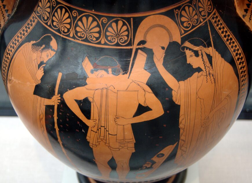 Hector receiving the helmet from Hecube (detail), Euthymides, Three Revelers depicting three figures engaged in a scene. The artwork features detailed red-figure style with ornamental patterns along the top, highlighting a central figure holding a shield and a helmet being presented by a robed woman.