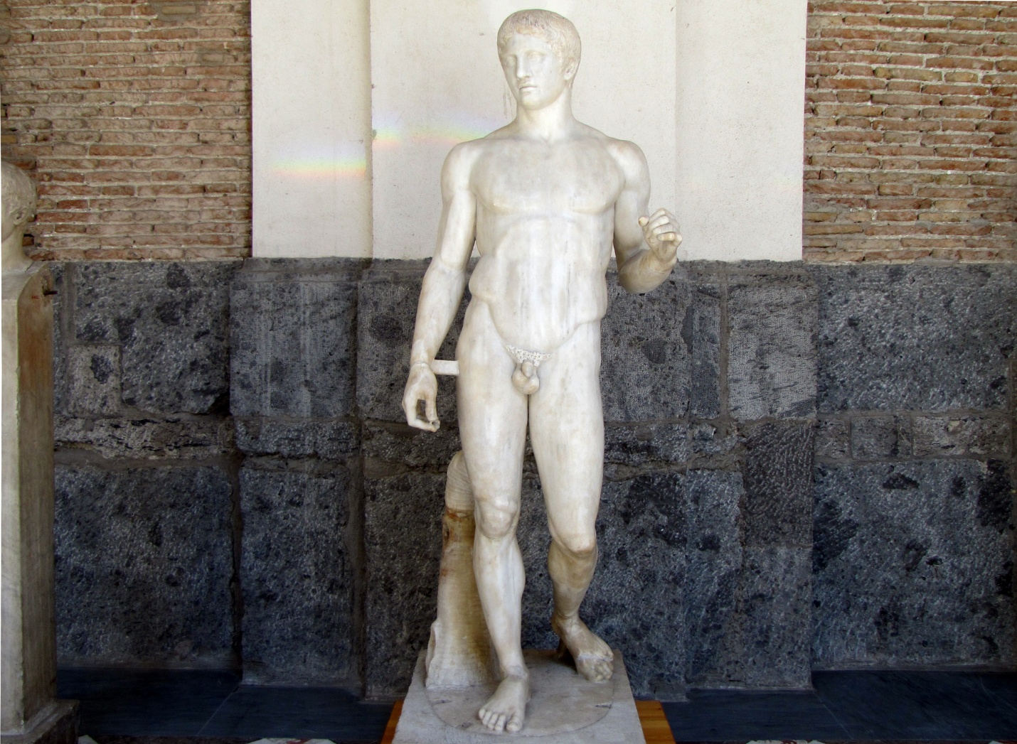 Polykleitos, Doryphoros (Spear-Bearer) nude youthful male sculpture carved from marble without paint on its current surface. The figure stands in contrapposto stance with his left arm lifted and bent at a 90 degree angle.
