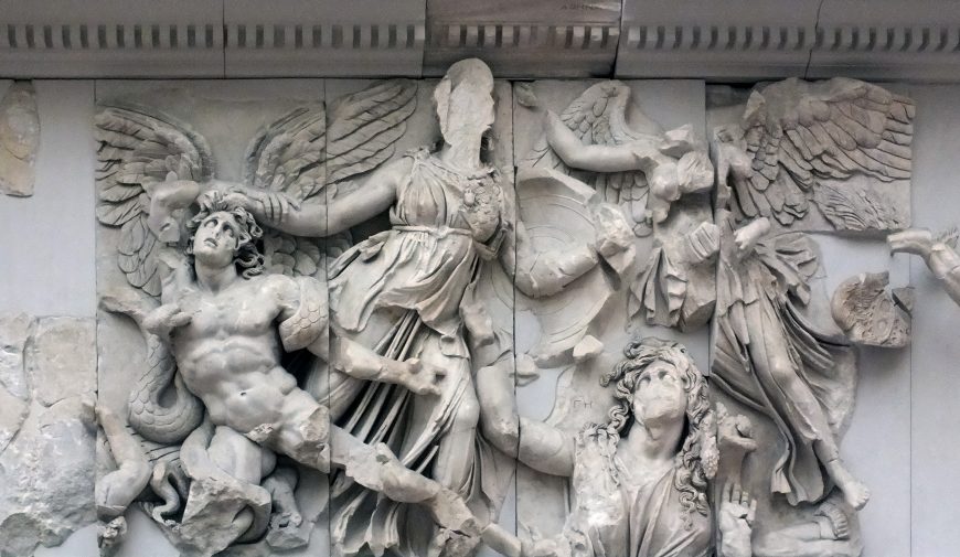 A detailed photograph of Athena defeats Alkyoneus (detail), The Pergamon Altar stone relief sculpture depicting mythological figures in dynamic poses with flowing garments and wings. The relief features intricate carvings of muscular human forms, serpents, and draped fabric, highlighting artistic craftsmanship and storytelling from classical antiquity.