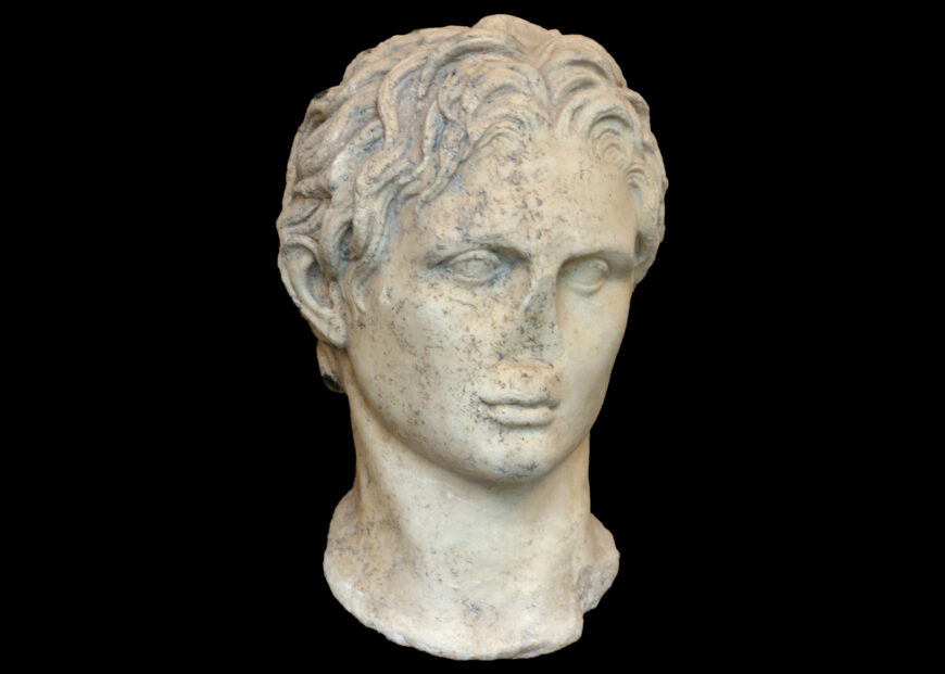 A photograph of Portrait of Alexander the Great marble bust sculpture depicting a Alexander the Great with curly hair, shown from the front against a black background. The bust includes detailed hair texture and a partial neck.