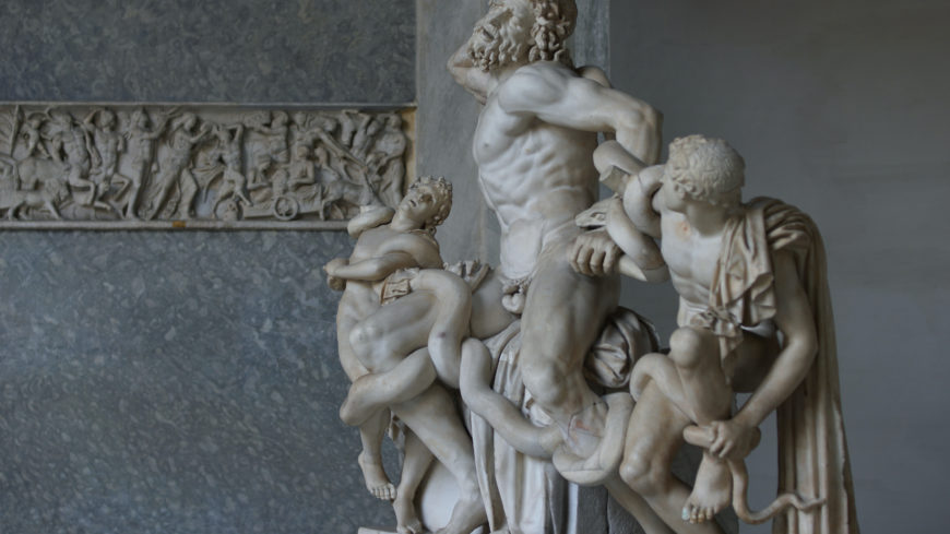 Side detail view of Laocoön and His Sons marble sculpture, depicting three human figures entwined by large serpents. The detailed composition highlights muscular anatomy, expressive faces, and intricate serpent coils, set against a plain background with a carved frieze visible on the left.