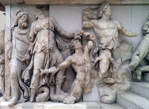 A photograph of an ancient marble relief sculpture depicting mythological figures in dynamic poses, including a central kneeling male figure and two standing figures on either side. The relief features intricate drapery, muscular details, and sea creatures at the base, with labels "NEREUS" and "OKEANOS" identifying the figures.