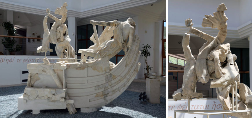 A photograph of a large, fragmented marble sculpture depicting multiple human figures on a boat, displayed indoors with natural light. The sculpture features dynamic poses and detailed anatomy, with visible cracks and missing parts, highlighting both artistic craftsmanship and signs of aging or damage.
