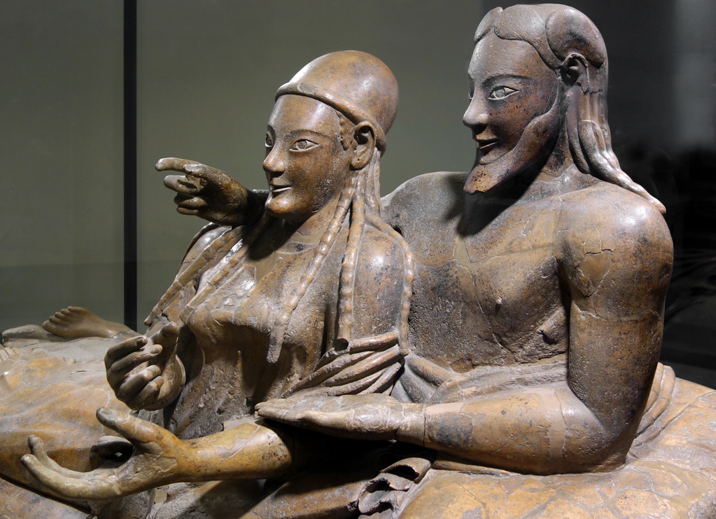 Upper bodies (detail), Sarcophagus of the Spouses, depicting a reclining couple on a cushioned couch, showcasing detailed carvings and lifelike poses. The sculpture highlights cultural aspects of Etruscan funerary art, with the couple likely holding objects.