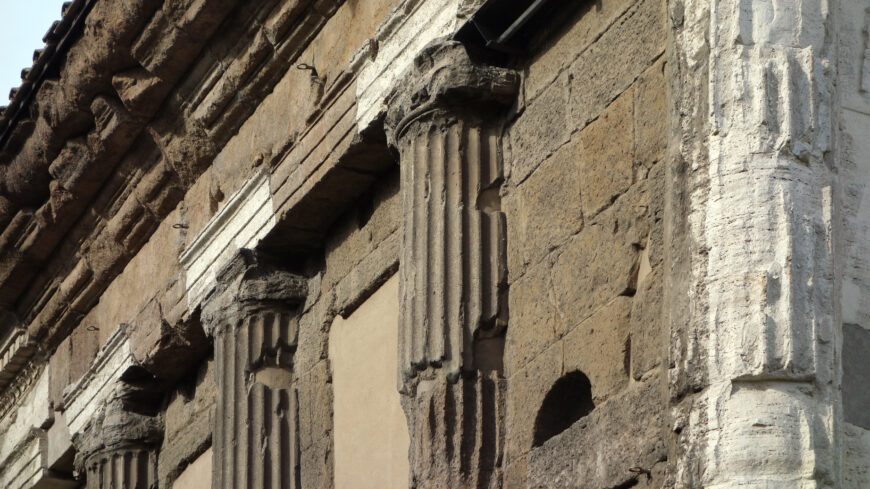 Photograph of an Engaged columns, Temple of Portunus with fluted shafts and capitals. The structure shows weathered textures and varying stone colors, highlighting historical architectural details and signs of aging.