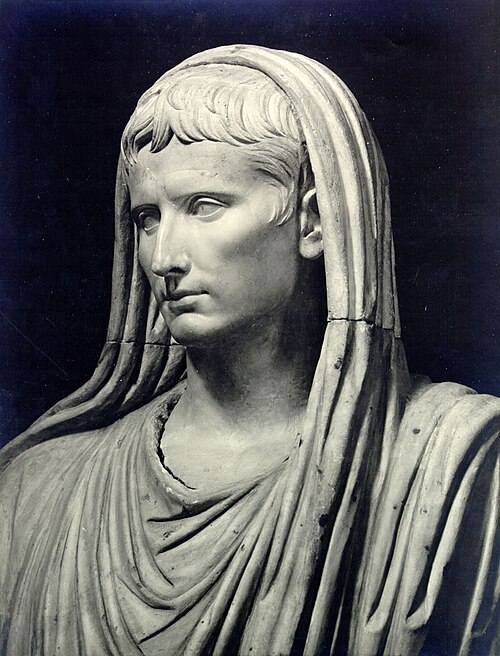 Photograph of a classical marble bust depicting a Roman figure wearing a toga with a hood draped over the head. The sculpture highlights detailed facial features and intricate folds in the garment, emphasizing solemnity and authority.