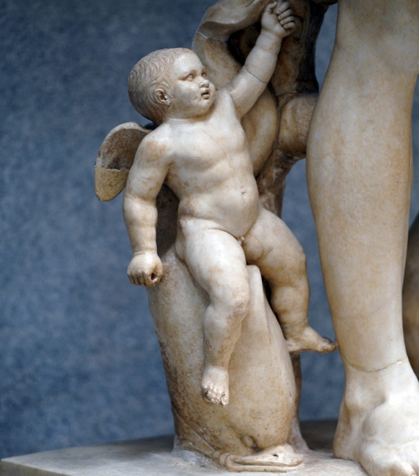 Photograph of a Cupid on a dolphin (detail), Augustus of Primaporta marble sculpture depicting a cherubic child with wings holding an adult's hand, standing on a base with a dolphin figure. The sculpture features detailed anatomy and smooth texture, highlighting artistic skill in representing human and mythical elements.
