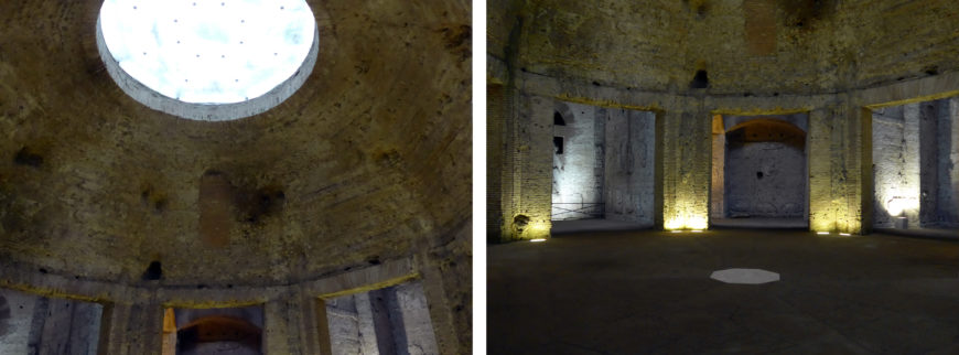 Photograph showing interior of a circular stone structure with a large round opening at the top allowing natural light inside. The space features evenly spaced arched doorways around the perimeter and subtle artificial lighting near the floor, highlighting the textured stone walls.