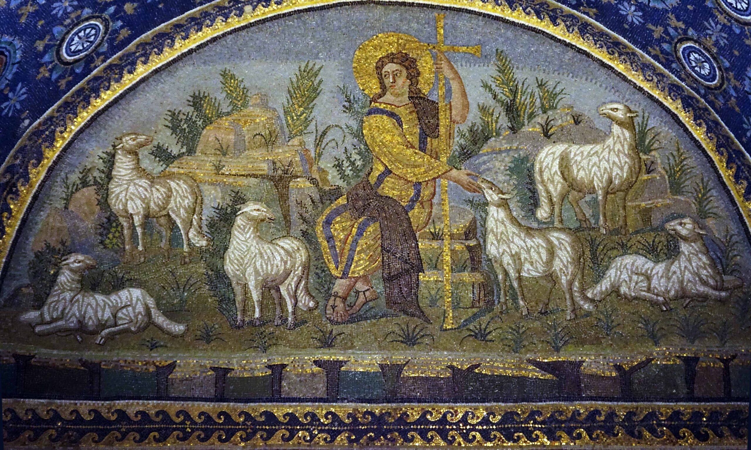 Mosaic artwork depicting a central Christ with a halo holding a cross staff, surrounded by six white sheep in a pastoral setting with plants and rocks. The scene uses gold, blue, and earth tones, framed by a decorative arch with intricate patterns and symbols.