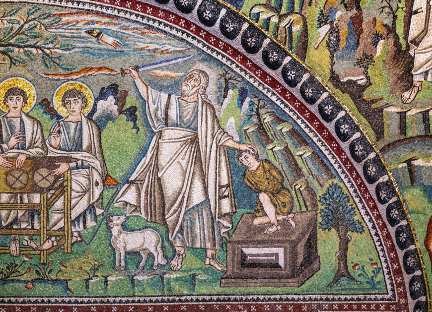 A colorful mosaic depicting a biblical scene with a central figure in white robes raising a hand over a kneeling child on an altar, accompanied by a lamb and two seated figures with halos. The mosaic features detailed greenery, birds, and a decorative border with circular patterns, illustrating a moment of sacrifice.