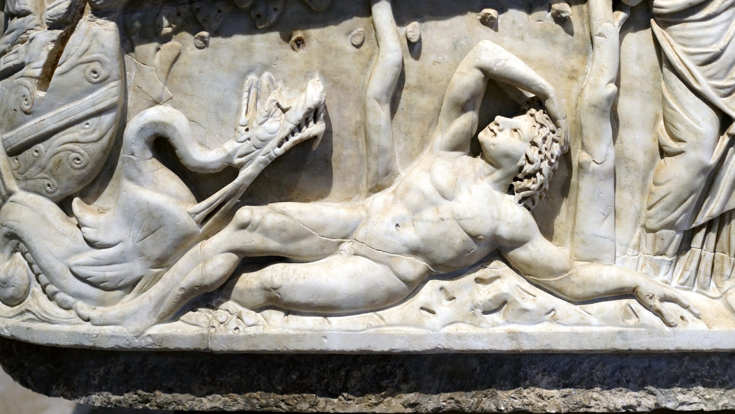A detailed marble relief sculpture depicting a muscular, reclining male figure with curly hair, seemingly in a struggle with a serpent-like creature. The scene includes intricate carvings of draped figures and ornamental elements, highlighting dynamic movement and classical artistic style.