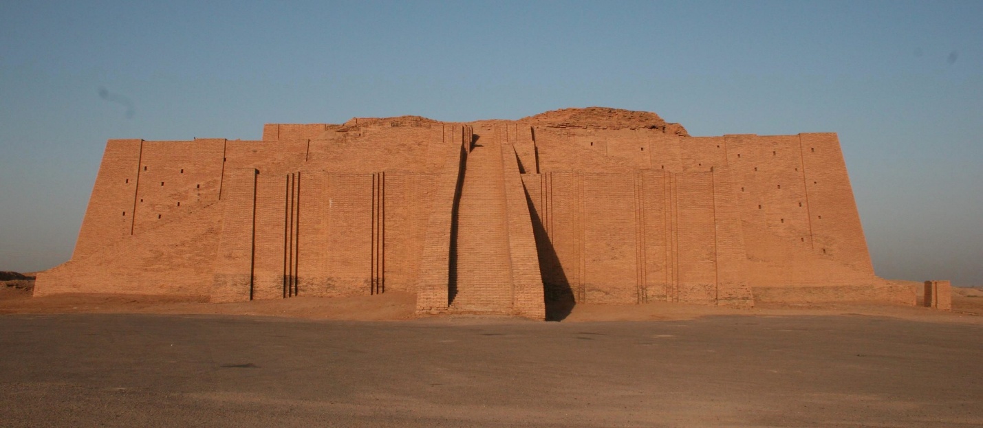 Photograph of an ancient ziggurat structure made of mud bricks, featuring a central staircase flanked by vertical grooves on a large rectangular facade. The structure is set against a clear sky with flat, barren ground in the foreground, highlighting its historical and architectural significance.