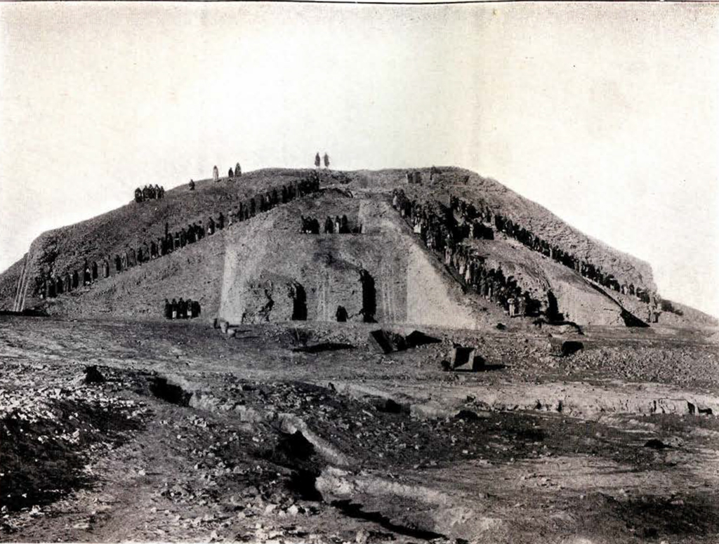 Black and white photograph showing a large ancient stepped ziggurat with groups of people standing along its terraces and summit. The barren surrounding landscape and attire of individuals suggest historical or archaeological significance of the site.