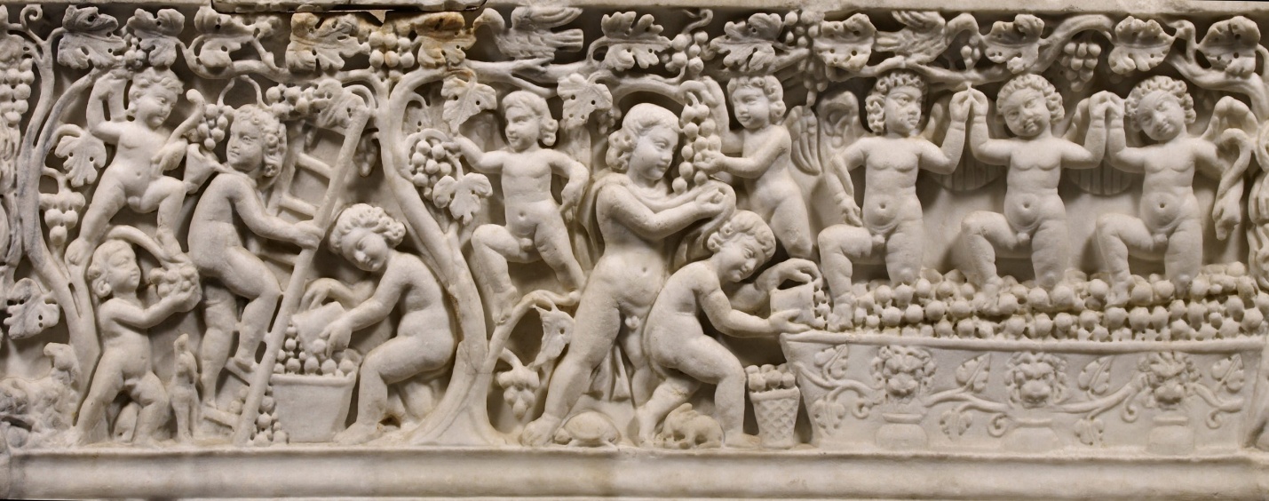 A detailed photograph of an ancient stone relief depicting multiple cherubic figures engaged in harvesting and gathering fruit. The relief features intricate carvings of trees, baskets, and floral motifs, highlighting a scene of abundance and communal activity.