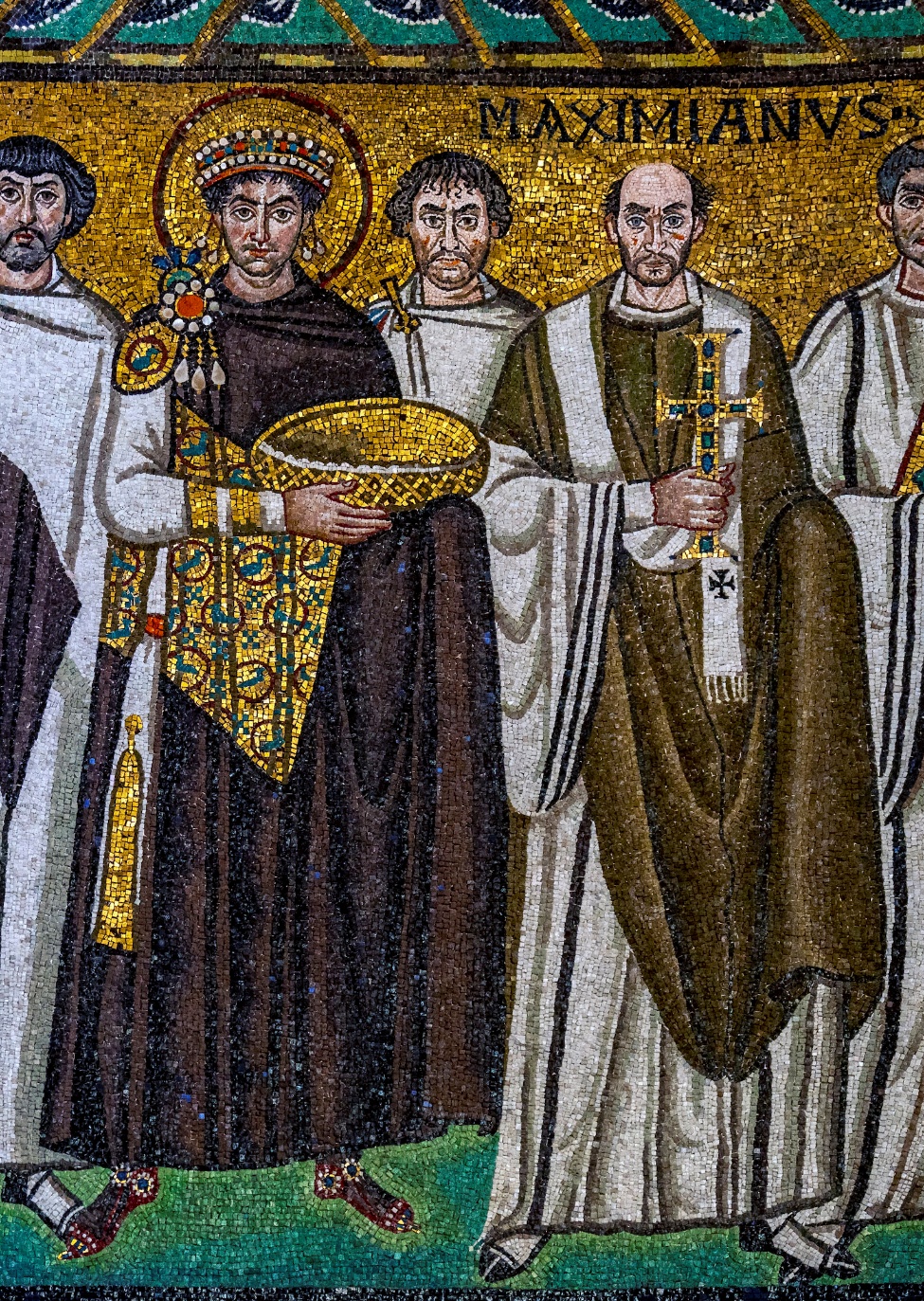 Detail of a mosaic artwork depicting a group of religious figures, including a crowned figure holding a golden bowl and a cleric holding a cross, labeled "MAXIMIANVS." The mosaic features detailed robes with intricate patterns and a gold background.