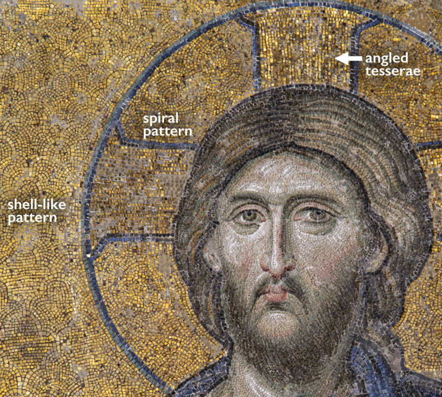 A close-up photograph of a mosaic artwork featuring a halo with distinct patterns labeled as shell-like, spiral, and angled tesserae. The mosaic uses gold and dark tones with blue outlines to highlight these intricate design elements within the circular halo structure.
