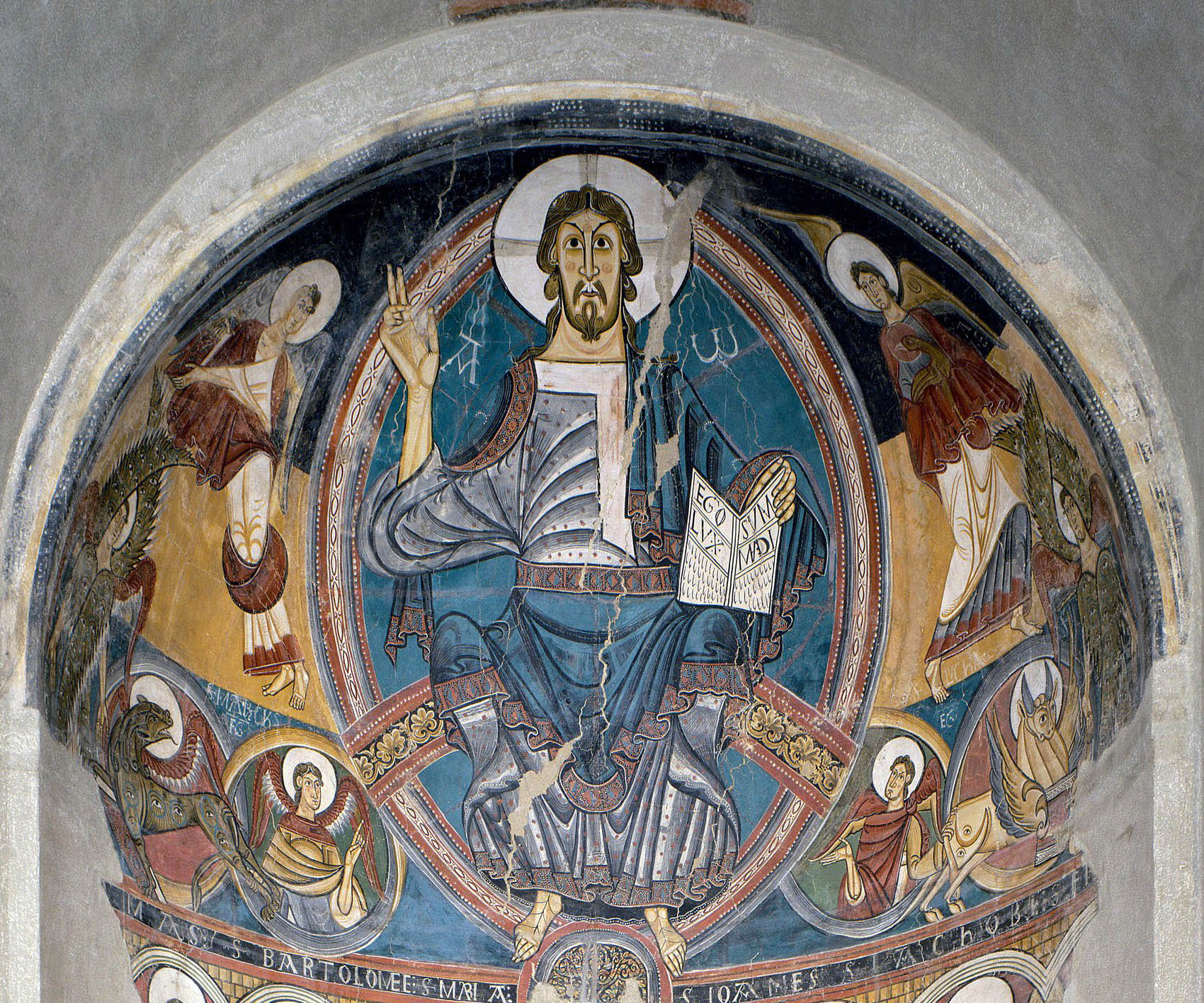 A fresco painting depicting a central figure seated on a throne with a halo, holding a book and raising one hand in blessing, surrounded by four angels in an arched frame. The artwork features vibrant colors including blue, red, and gold, with Latin inscriptions and intricate detailing typical of medieval religious art.