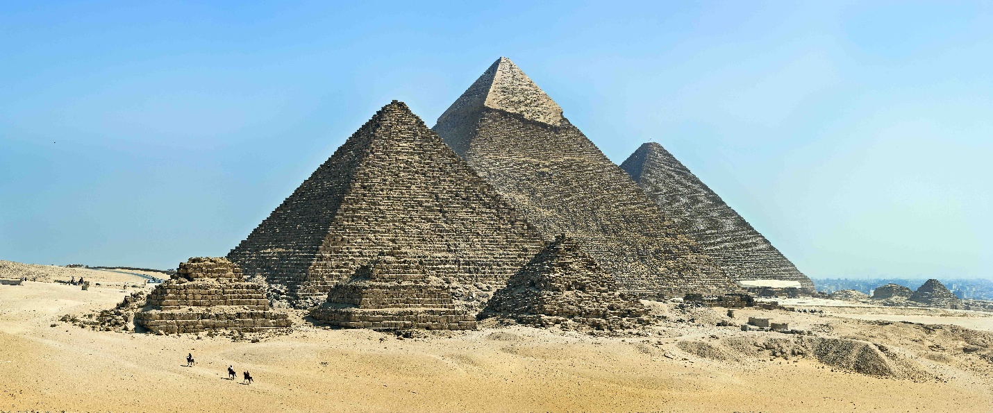 Photograph of Great Pyramids of Giza in Egypt showcasing three large pyramids with smaller pyramids in foreground under clear blue sky. Sand dunes surround pyramids, highlighting ancient architectural marvels and historical significance as one of world's oldest and largest pyramid complexes.