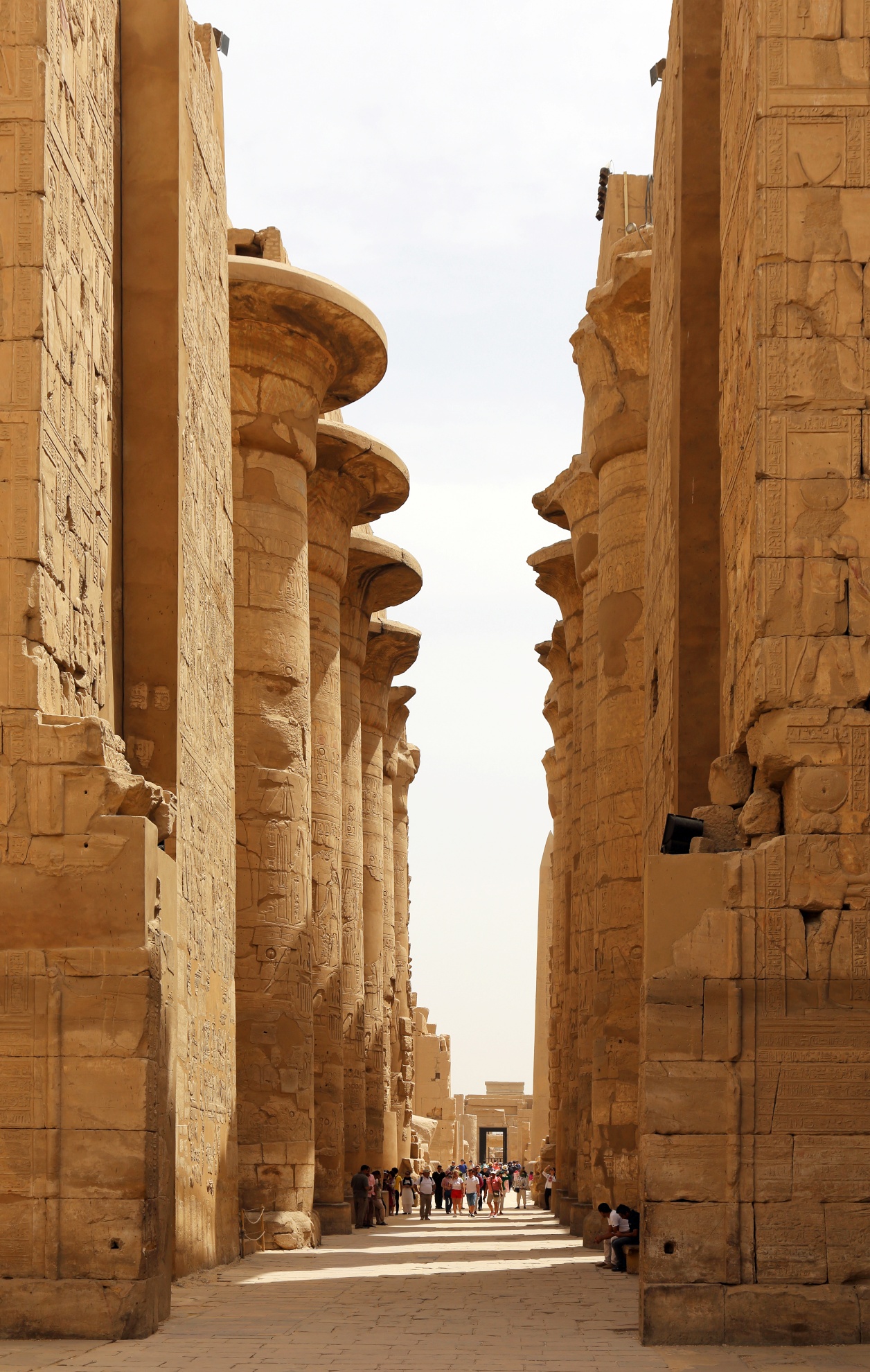 Photograph of Hypostyle hall from Karnak with ancient stone columns arranged in rows within a large open structure, showcasing intricate carvings and hieroglyphs on the surfaces. Columns vary in size and detail, with light filtering through gaps, highlighting architectural grandeur and historical significance.