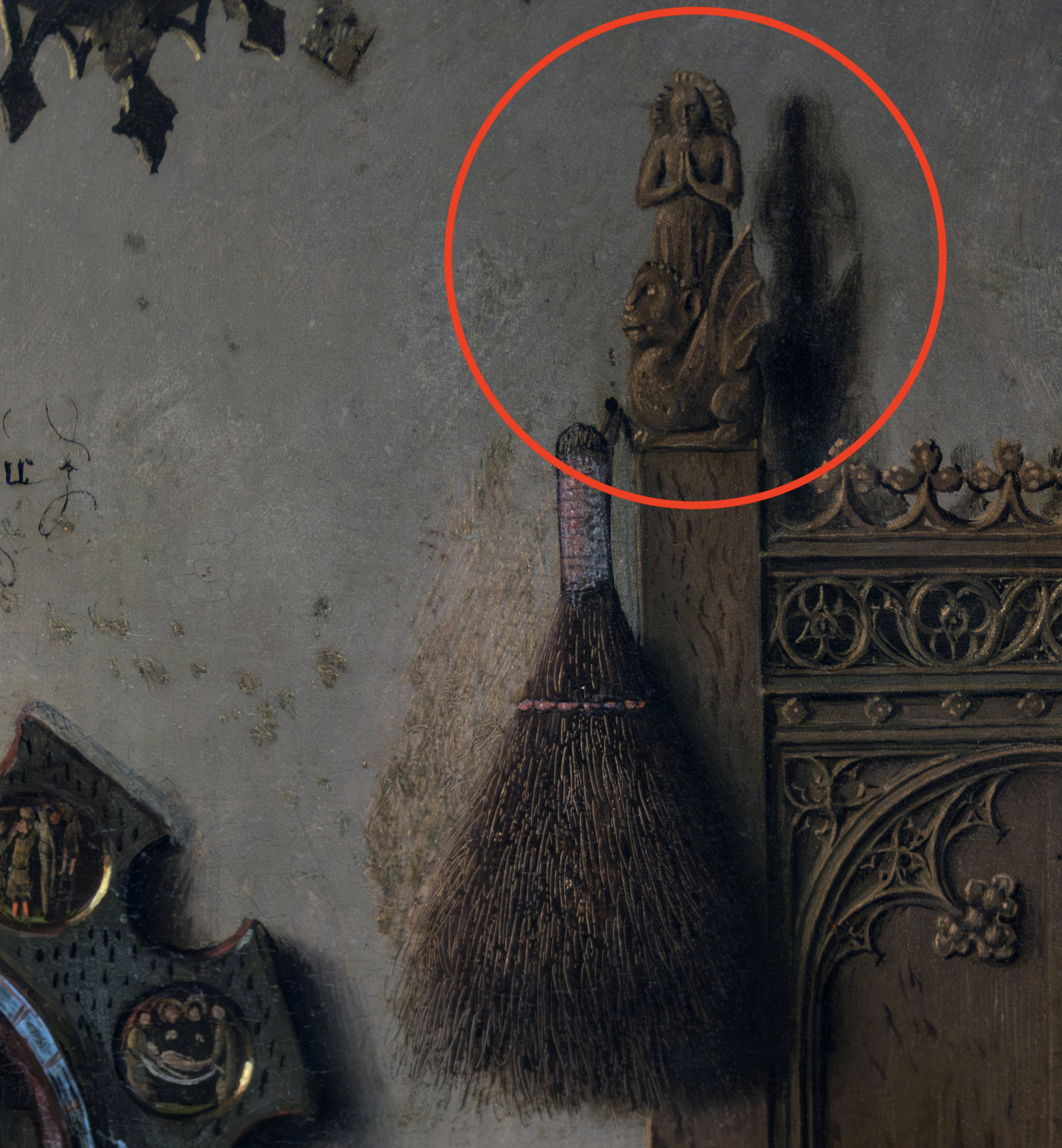 Photograph of a detailed section of a carved wooden panel featuring a small angelic figure with hands clasped in prayer atop a decorative post, highlighted by a red circle. The panel includes intricate floral motifs and a broom leaning against it, showcasing fine craftsmanship and religious symbolism.