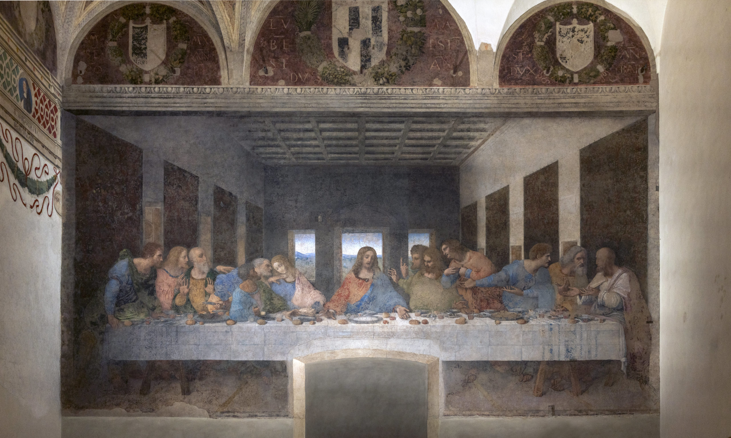 Leonardo da Vinci's Last Supper depicting a long dining table with Jesus Christ at the center surrounded by his twelve apostles during the Last Supper. The artwork features detailed expressions, a muted color palette, and architectural elements like arched windows and a coffered ceiling.