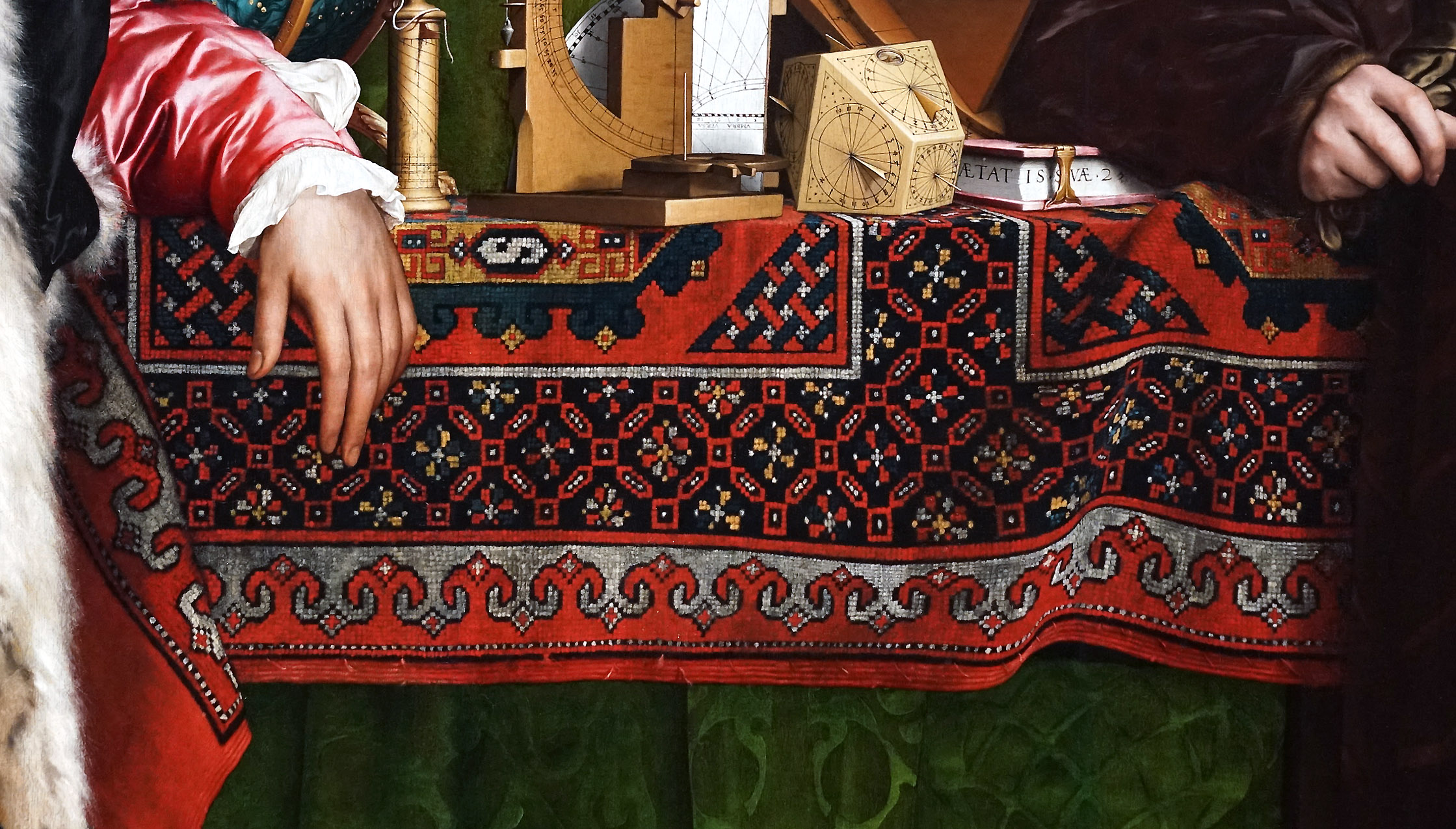 Carpet (detail), Hans Holbein the Younger, The Ambassadors showing two hands resting on an ornately patterned red and black textile draped over a table. The scene includes scientific instruments like a globe and a polyhedral sundial.